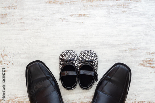 Father's business black shoes and daughter's baby black shoes on rustic white wood background. Concept of family, single parent and father's day. Flat lay top view with copy space.