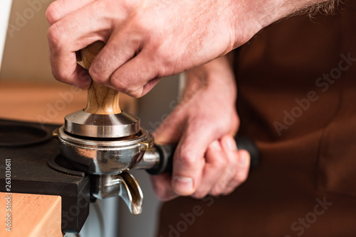 Partial view of barista in brown apron preparing coffee
