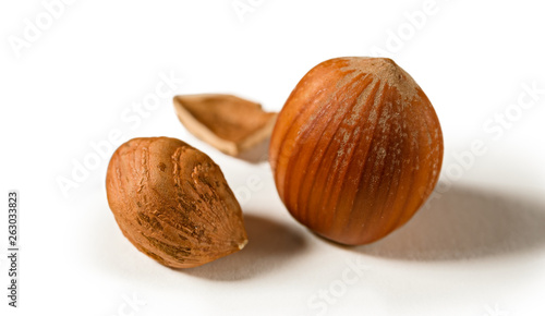 A shelled hazelnut with fragments of its shell around it, isolated on a white background