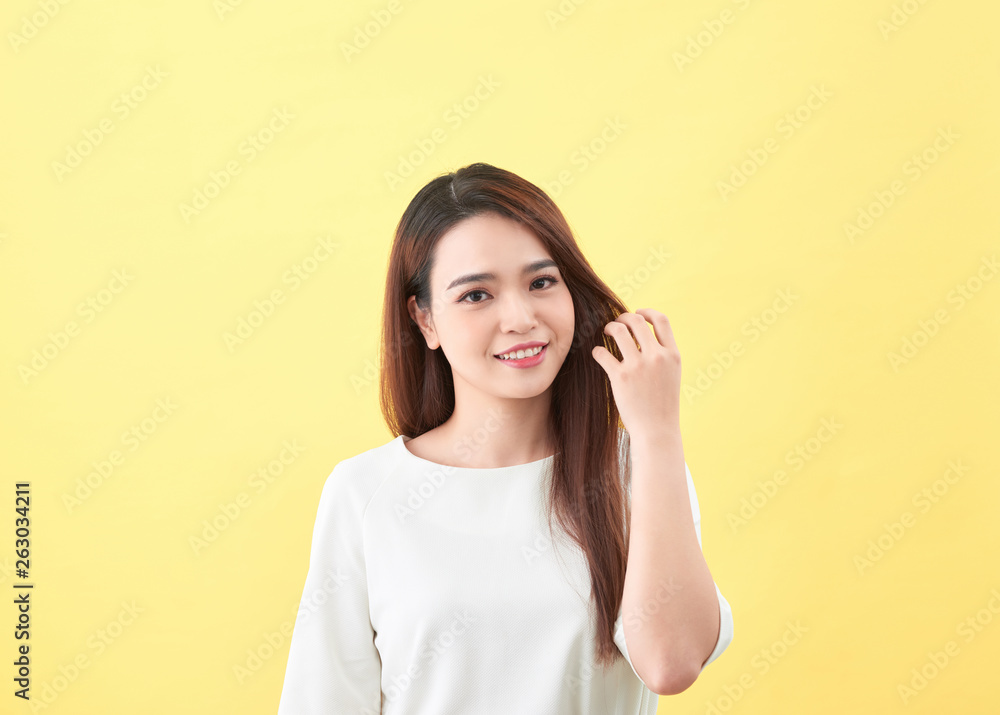 Asian young beautiful woman smiling and touching smooth her hair on yellow background Asian young beautiful woman smiling and touching smooth her hair on yellow background