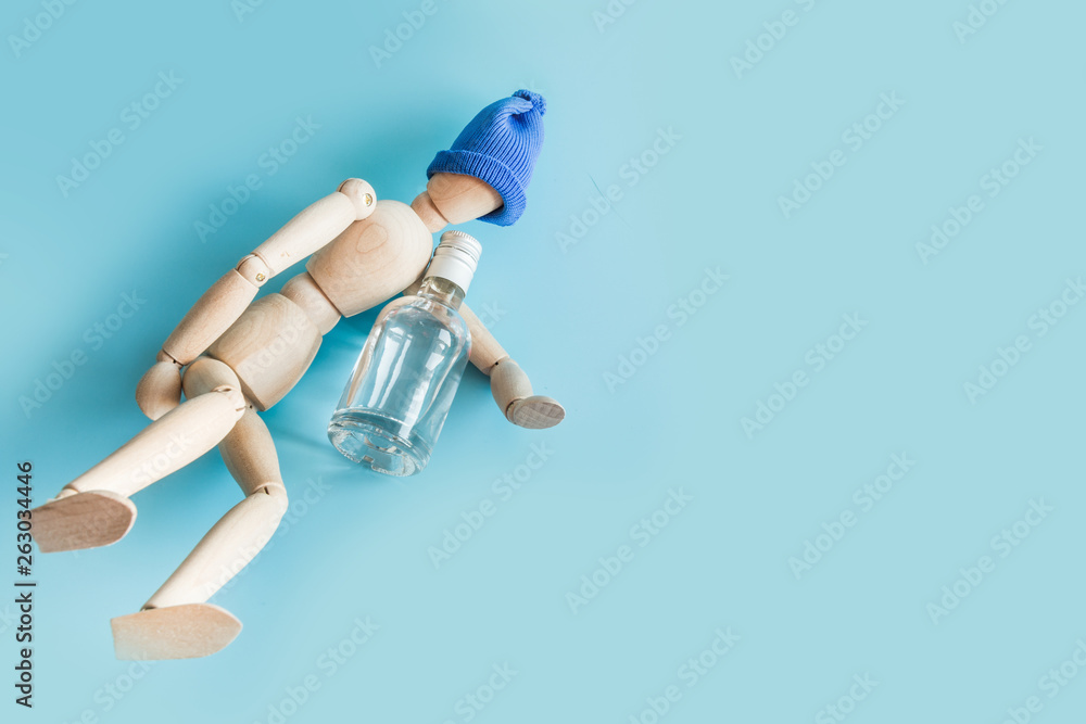 Wooden doll with bottle of vodka on blue. Concept harm of alcohol. Space for text.