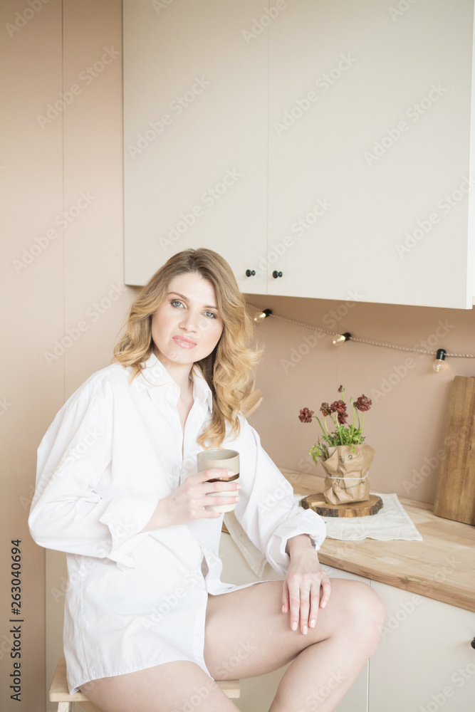 beautiful blonde girl in the kitchen with a cup of coffee or tea in her hands
