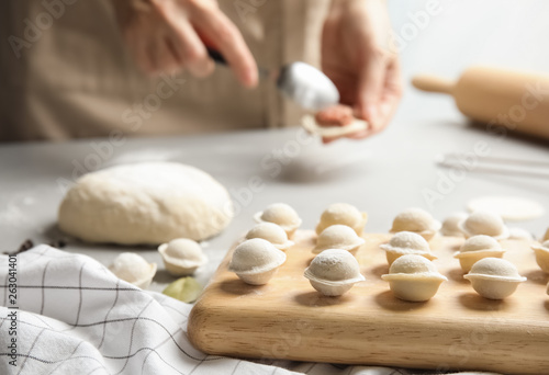 Wooden board with raw dumplings and blurred woman on background, closeup