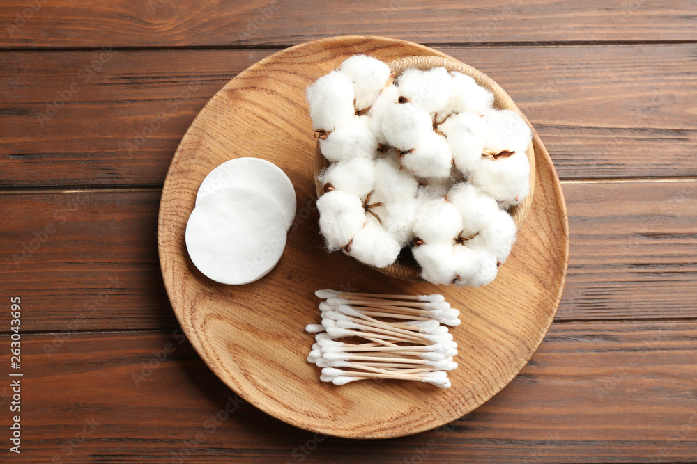 Plate with cotton swabs, pads and flowers on wooden background, top view Plate with cotton swabs, pads and flowers on wooden background, top view
