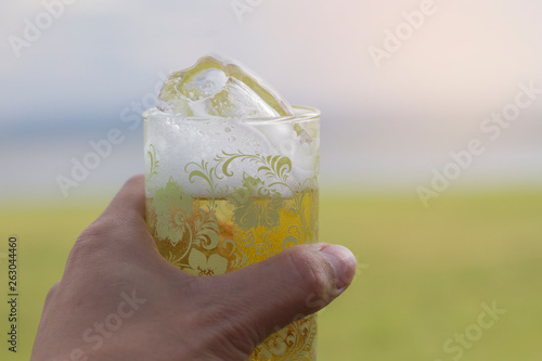 Male hand holds a glass of beer with ice and the nature of the mountain and the evening sky as the background.