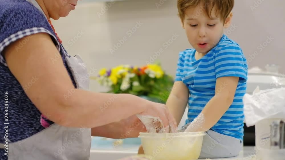Close up of the happy smiled grandmother and grandson kneading a daugh together. slow motion of an elderly woman and little boy preparing pasta or pizza together. Close up of the happy smiled grandmother and grandson kneading a daugh together. slow motion of an elderly woman and little boy preparing pasta or pizza together.