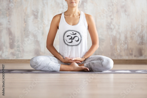 Attractive young woman in cotton suit practices yoga and meditates sitting on a rug on the floor In a spacious bright room close up photo