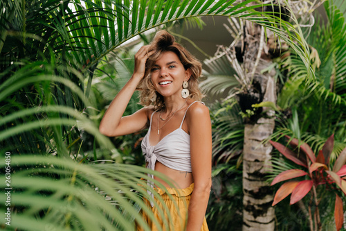 Attractive caucasian blond woman with curly blond hair walking outside in exotic green park and posing to camera #263054850