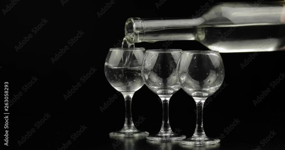 Pouring up three shots of vodka from a bottle into glass. Black background Pouring up three shots of vodka from a bottle into glass. Black background