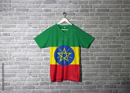Ethiopia flag on shirt and hanging on the wall with brick pattern wallpaper. © Achisatha