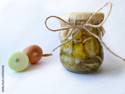 Tableau sur toile Salad of pieces of pickled cucumbers and onions in a glass jar and two bulbs on a light background