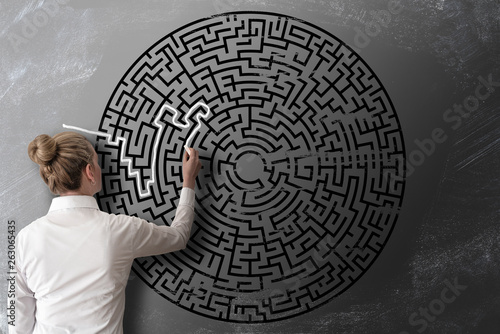 woman trying to find way through chalk drawing of maze on blackboard challenge concept photo