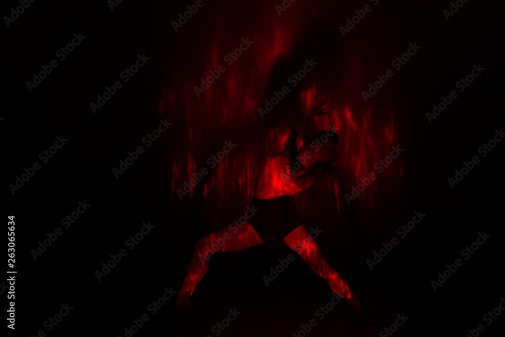 Beautiful dancer moving her body in front of and red light while performing a perfect dance composition of moves. The dance scene is showing off the inferno in a spectacular way., long exposure motion