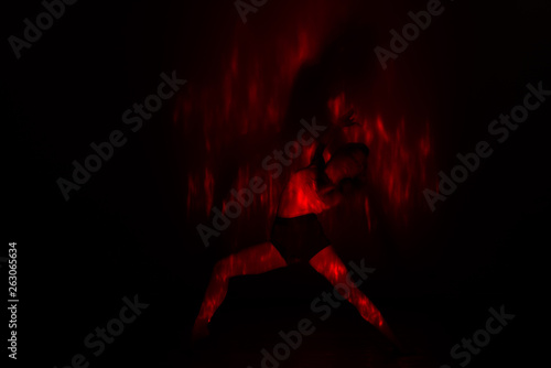 Beautiful dancer moving her body in front of and red light while performing a perfect dance composition of moves. The dance scene is showing off the inferno in a spectacular way., long exposure motion