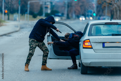 The car thief is pulling the car owner out of his car and trying to get the car while pointing a loaded gun at the drivers head.. photo