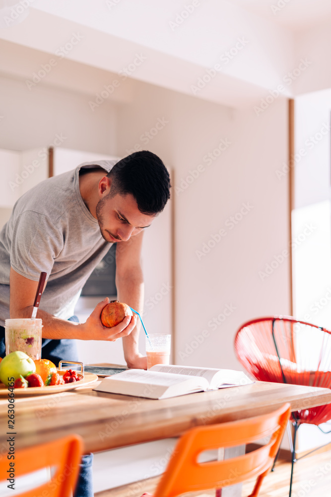 healthy strong young man reading a book early in the morning while making his smoothie. healthy strong young man reading a book early in the morning while making his smoothie.