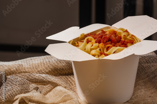 Homemade Pasta, Noodles, fettuccine Alfredo or Bolognese for take away in a white box on a wooden background close up shot. place for logo or copy paste text