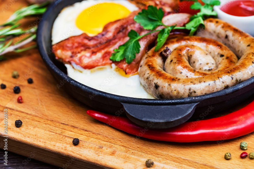 Nutritious meal with fried egg, sausage, bacon, tomato and sauce in frying pan Nutritious meal with fried egg, sausage, bacon, tomato and sauce in frying pan
