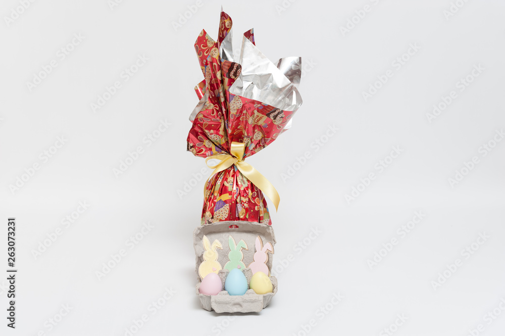 Easter egg in lovely red packaging with yellow ribbon and several small colorful eggs with ornament bunnies. Isolated on white background. Copy space.