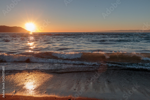 Wet sand foreground and approaching waves at sunset