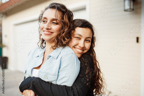 Картината върху платно Portrait of smiling daughter embracing mother while standing against house in ya