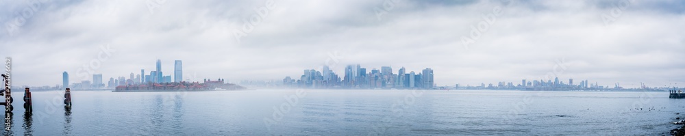 Panoramic New York City skyline with dramatic low clouds including Jersey City, Manhattan, and Brooklyn as seen from Liberty Island