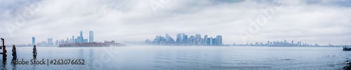 Panoramic New York City skyline with dramatic low clouds including Jersey City, Manhattan, and Brooklyn as seen from Liberty Island