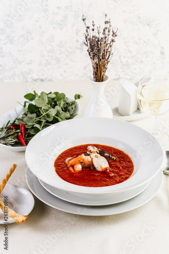 Delicious tomato clam chowder soup with shellfish, shrimps, squid, mussels, octopus and seafood close-up on a in a white bowl on the on a served white table