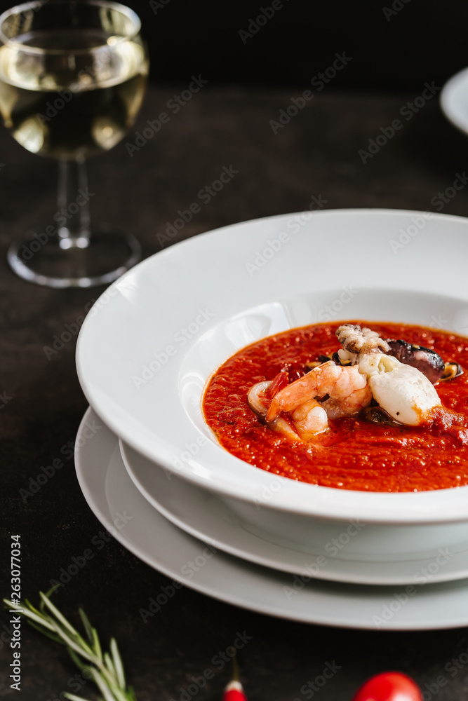 Delicious tomato clam chowder soup with shellfish, shrimps, squid, mussels, octopus and seafood close-up on a in a white bowl on the served black table Delicious tomato clam chowder soup with shellfish, shrimps, squid, mussels, octopus and seafood close-up on a in a white bowl on the served black table