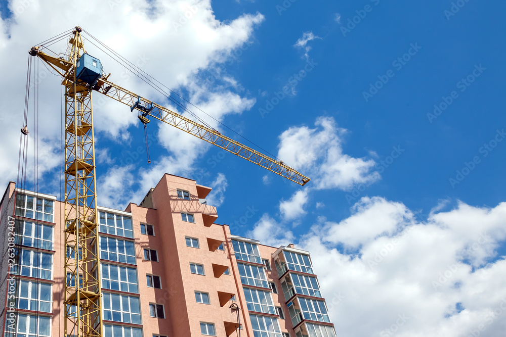 Tower crane  building new modern  apartment house on a background of blue cloudy sky at sunny day. Real estate concept.