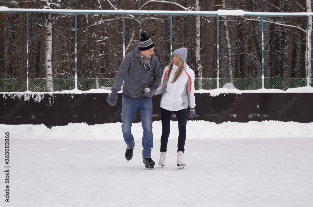 Young couple skating at a public ice skating rink outdoors in the city