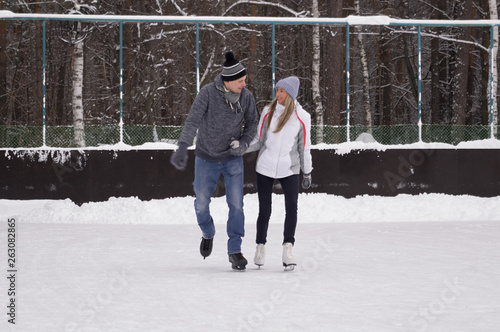 Young couple skating at a public ice skating rink outdoors in the city