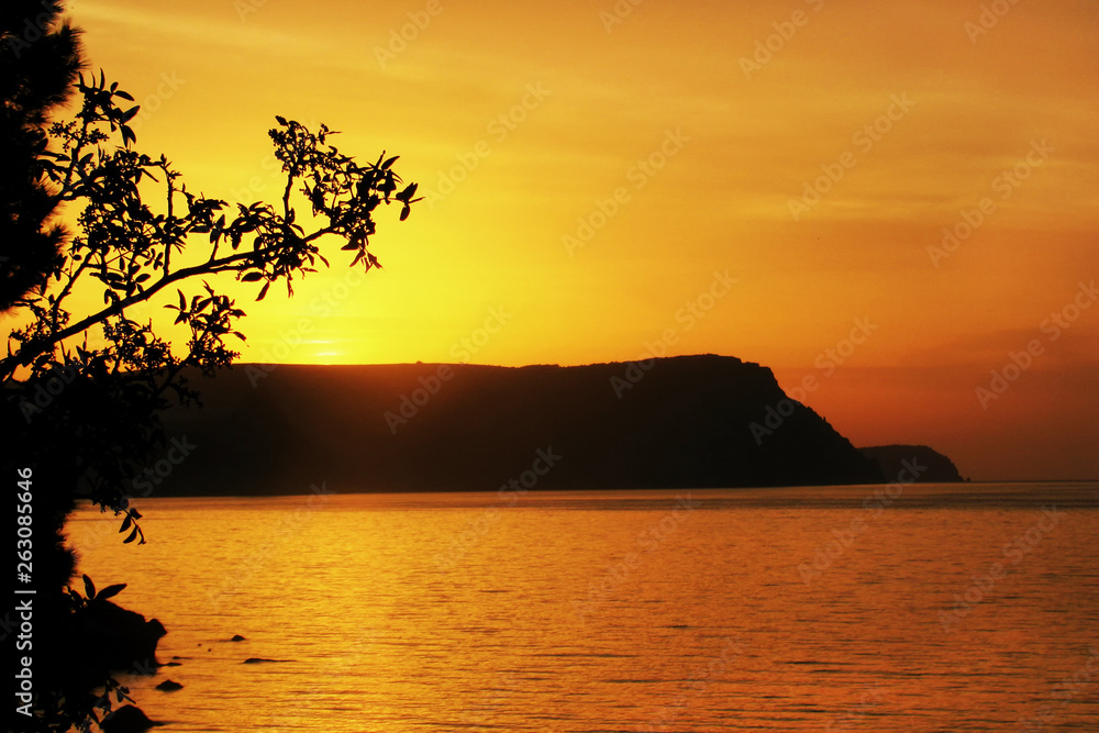 Orange sunset over sea. Sun sets beautifully over ridge of mountain. Seascape with a silhouette of a hill in Bay. Orange sunset over sea. Sun sets beautifully over ridge of mountain. Seascape with a silhouette of a hill in Bay.