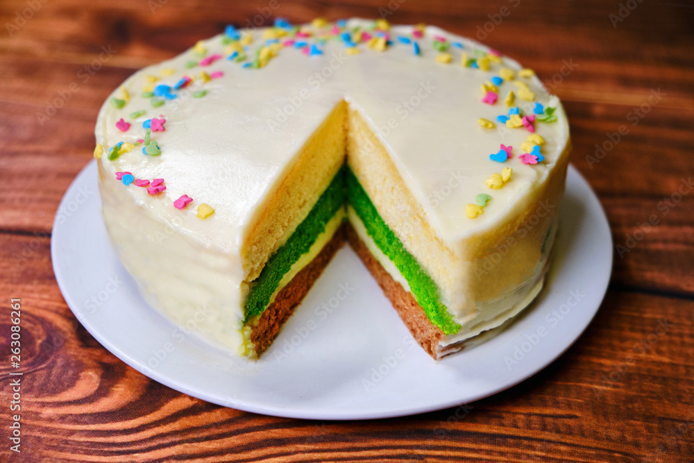 Three-color cake on a wooden table. A plate of dessert with layers of green, brown and white. Sprinkled with candy and soaked with sweet cream baking. White sponge cake. Three-color cake on a wooden table. A plate of dessert with layers of green, brown and white. Sprinkled with candy and soaked with sweet cream baking. White sponge cake.