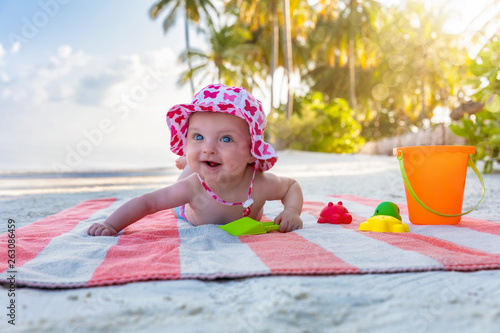 Süßes Baby mit Sonnenhut spielt am tropischen Strand mit seinen bunten Spielsachen