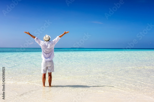 Mann in weißer Sommerkleidung steht am tropisch Strand und genießt die Freiheit
