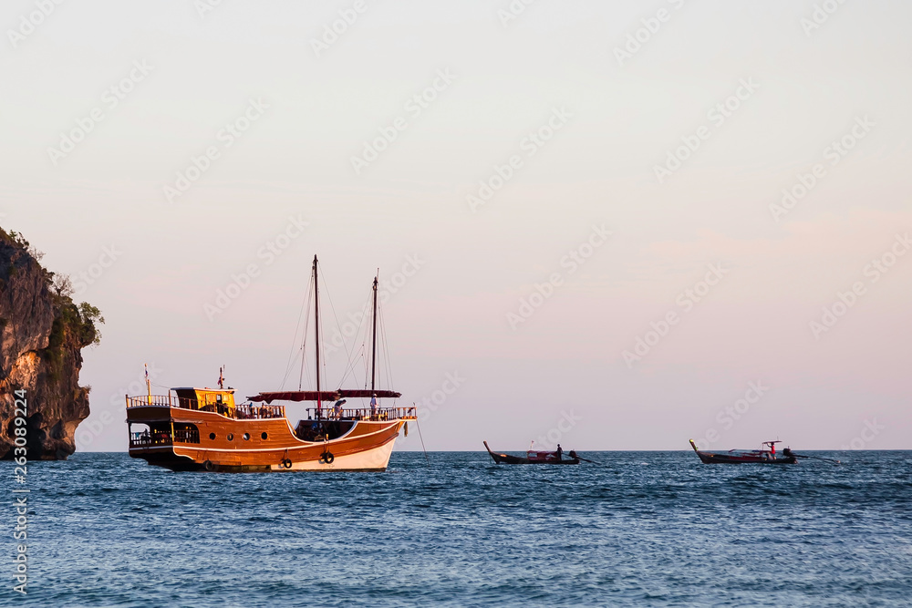 Sailing wooden ship in the old style sails on the sea. Nearby there are two small long-haul boats.