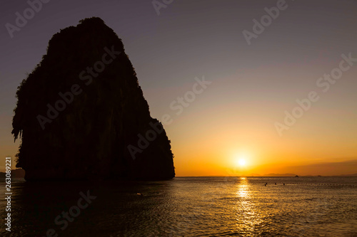 Beautiful golden sunset on the Phra Nang beach at Krabi in Thailand. Sandy beach and people swimming in the water. Cave mountain at the left