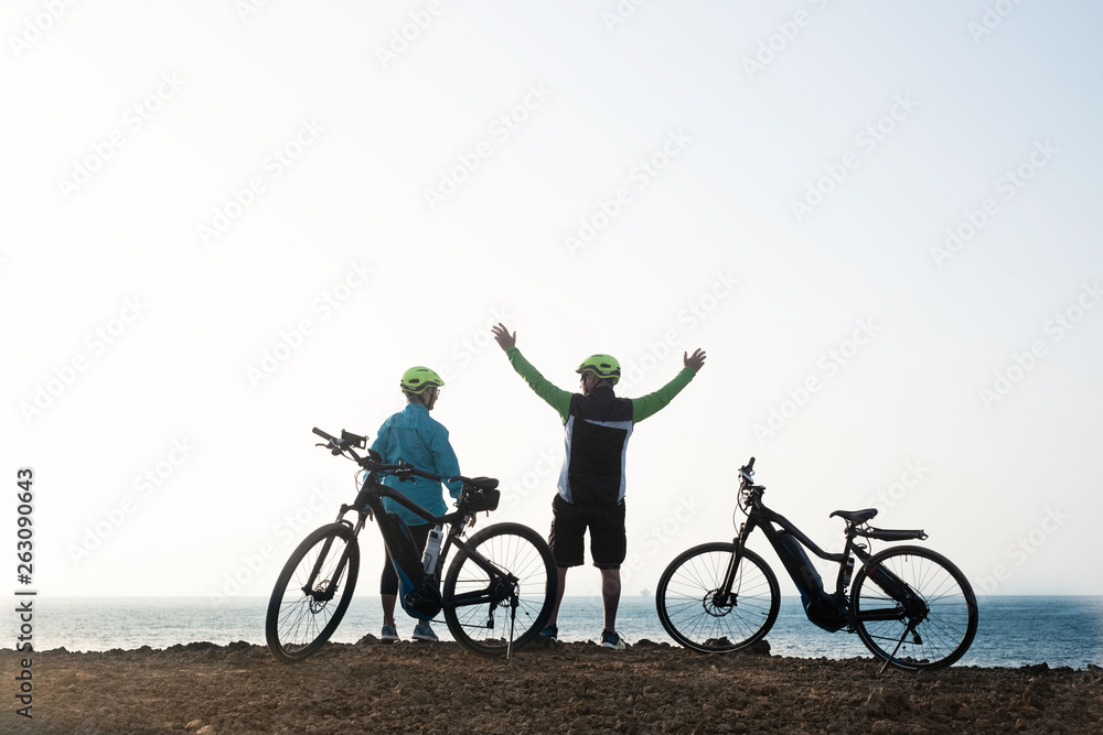 Obraz premium Two people enjoy the view of the ocean resting after an excursion with the bicycles. Cliff of volcanic landscape