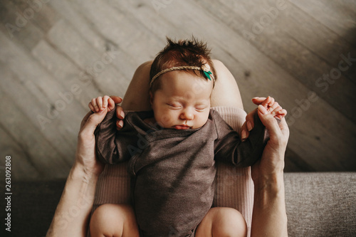 Mother is holding newborn baby on her knees. The kid is sleeping. 