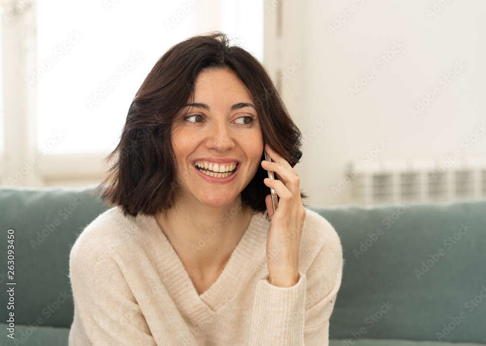 Happy young woman talking on smart phone sitting on sofa at home. In leisure and technology Happy young woman talking on smart phone sitting on sofa at home. In leisure and technology
