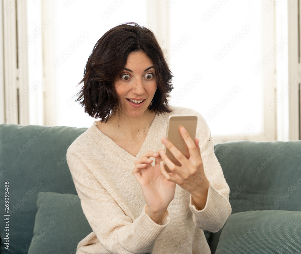 Happy young woman using her smart phone sitting on sofa at home. In leisure and mobile addiction Happy young woman using her smart phone sitting on sofa at home. In leisure and mobile addiction