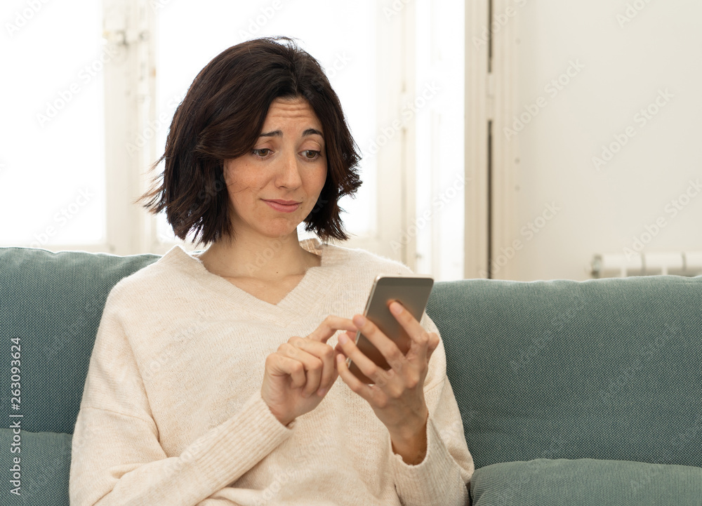 Happy young woman using her smart phone sitting on sofa at home. In leisure and mobile addiction Happy young woman using her smart phone sitting on sofa at home. In leisure and mobile addiction