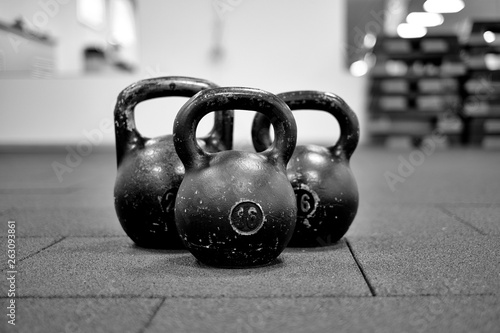 Fototapeta Naklejka Na Ścianę i Meble -  Тhree black iron kettlebells with markings 24 and 16 kg standing close to each other. Gym and fitness equipment. Workout tools. Black and white image