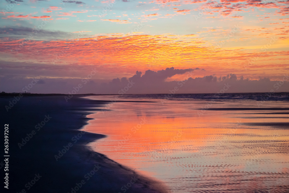 All the colors of sunrise are reflected on the water at low tide, with the beach still in deep shadow.