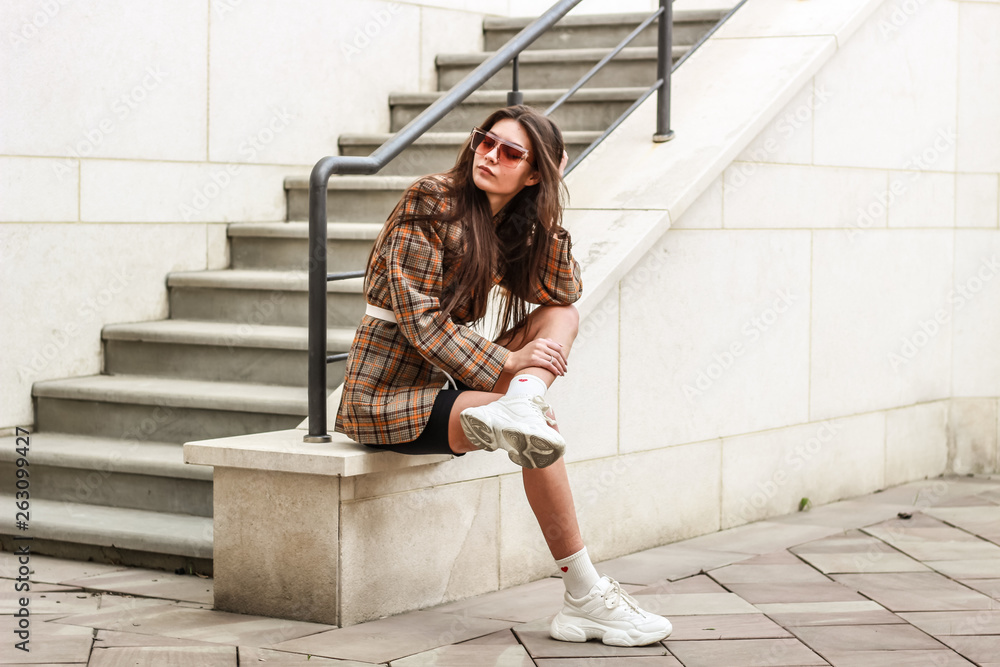 Portrait shooting of a stylish girl. Beige shades. Trends of spring and summer 2019. Wide jacket and belt leather bag. White sneakers and bike shorts - obrazy, fototapety, plakaty 