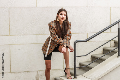 Portrait shooting of a stylish girl. Beige shades. Trends of spring and summer 2019. Bike shorts. Thick cloak, cover jacket. Gold earrings. Heels