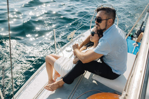 A girl and a guy of Asian appearance are sitting on the deck of the yacht, embracing each other. The couple looks to the horizon. © Svyatoslav Balan