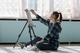 The girl artist is sitting on the floor of marble tiles. Woman in the process of drawing oil paintings.
