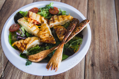 Grilled Halloumi Cheese salad witch tomatoes and lettuce in white plate in wooden background. healthy food